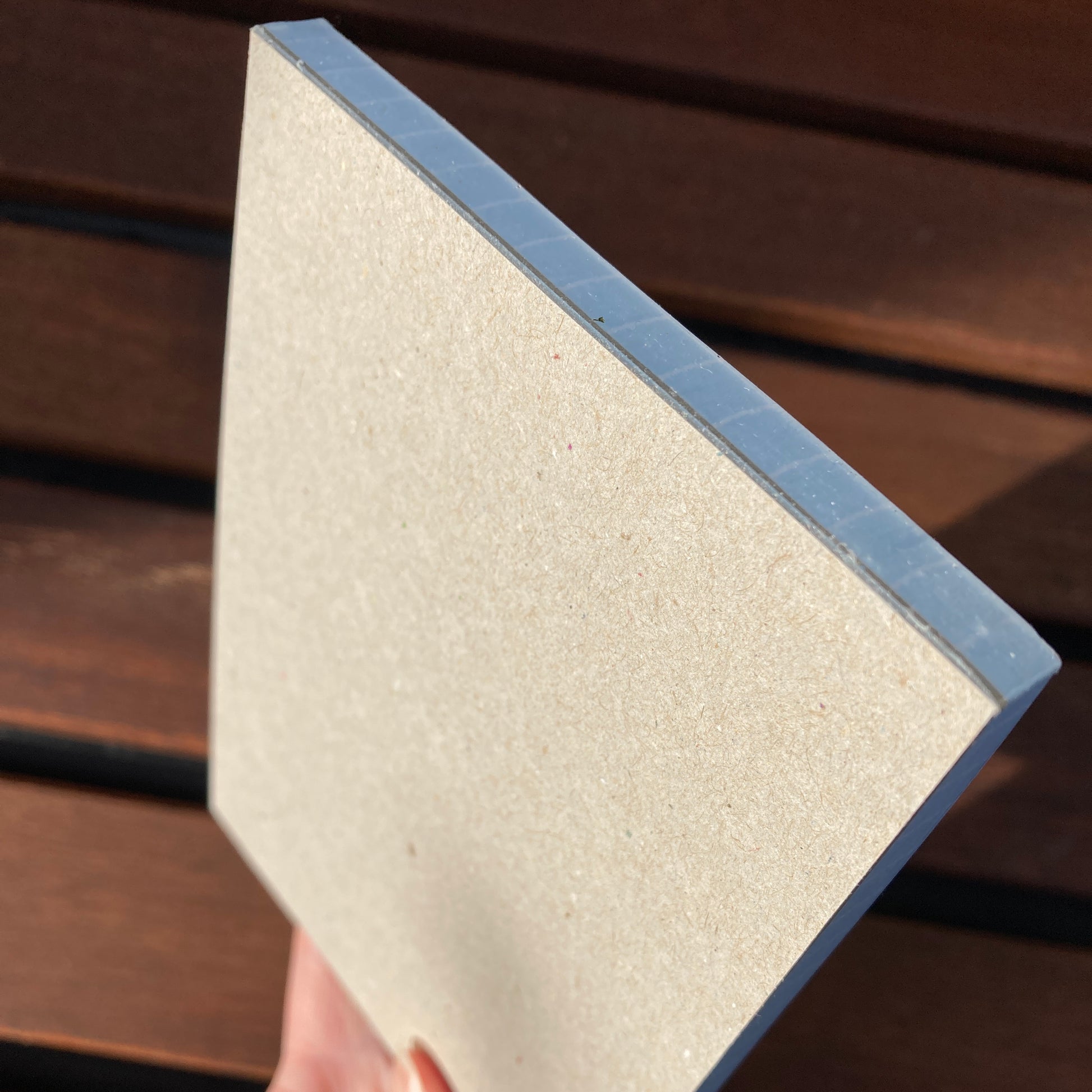 A hand holding the notepad at an angle to show the brown greyboard back of the notepad.