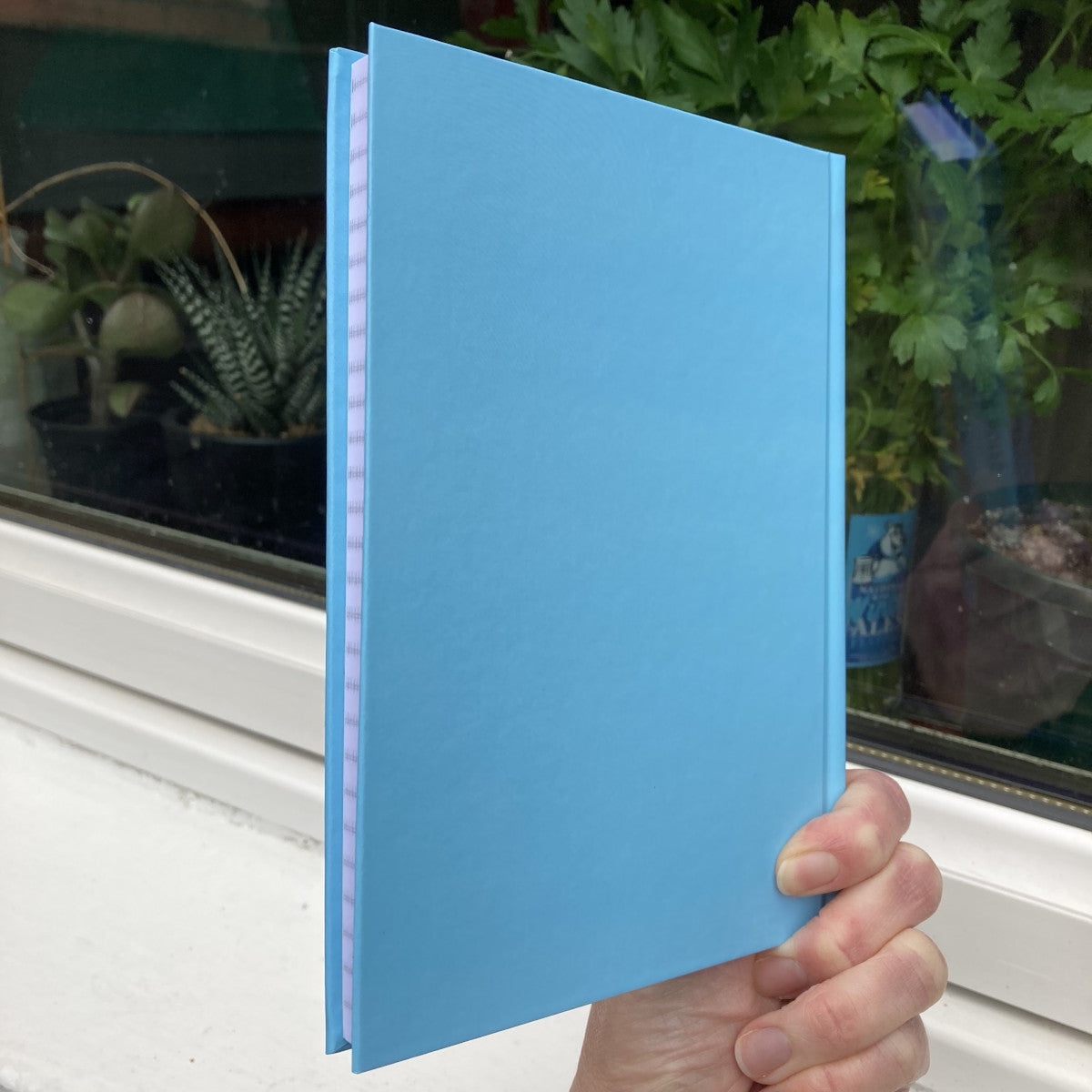 Blue hardback journal held showing the back