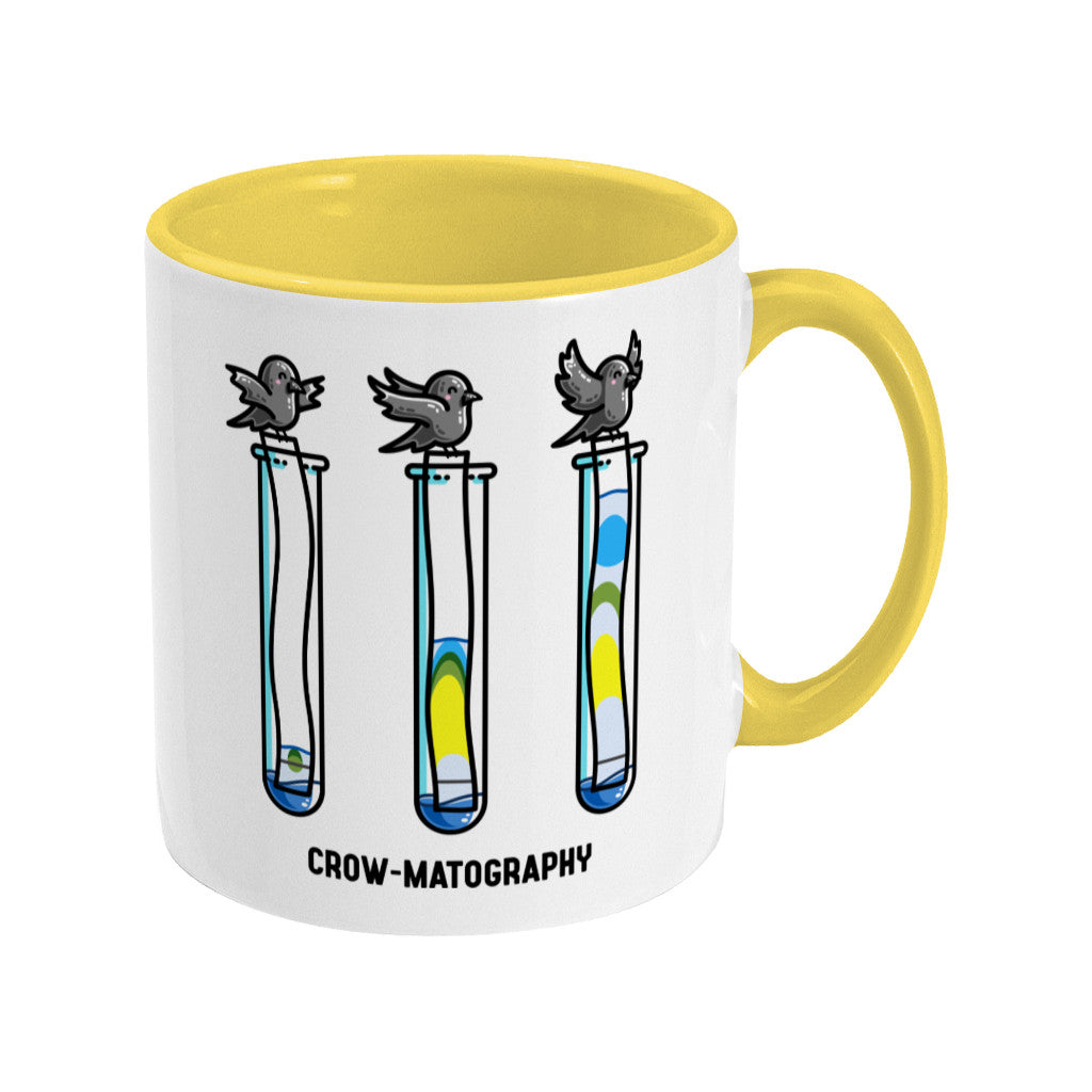A two toned white and yellow ceramic mug with the handle to the right showing a design of 3 crows holding strips of paper into 3 test tubes showing colour separation.