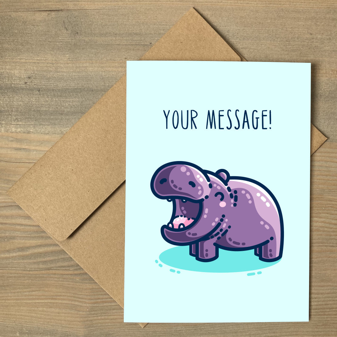 A large pale turquoise greeting card lying flat on a brown envelope. On the card is a kawaii cute purple hippo with a thick dark blue outline, seen side on facing to the left with its happy mouth open wide. There is a dark turquoise shadow beneath the hippo and thin upper case dark blue personalised text above