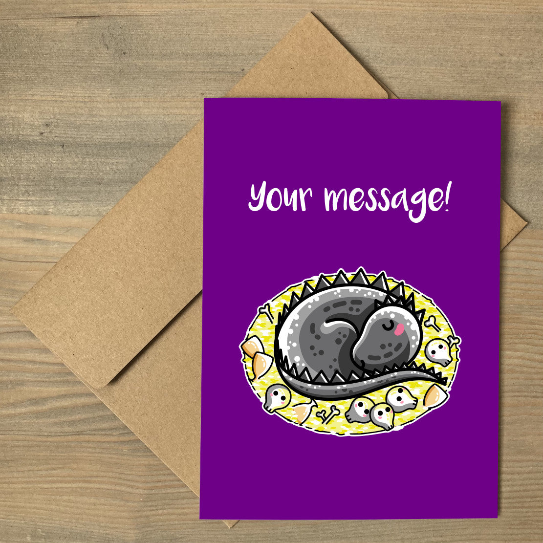Personalised purple greeting card lying flat on a brown envelope with a design of a cute grey dragon curled on its treasure hoard with the personalised words Your message written above