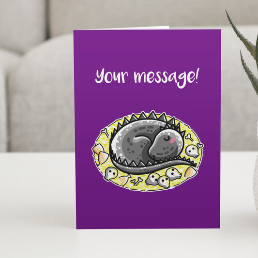 Personalised purple greeting card standing on a white table with a design of a cute grey dragon curled on its treasure hoard with the personalised words Your message written above