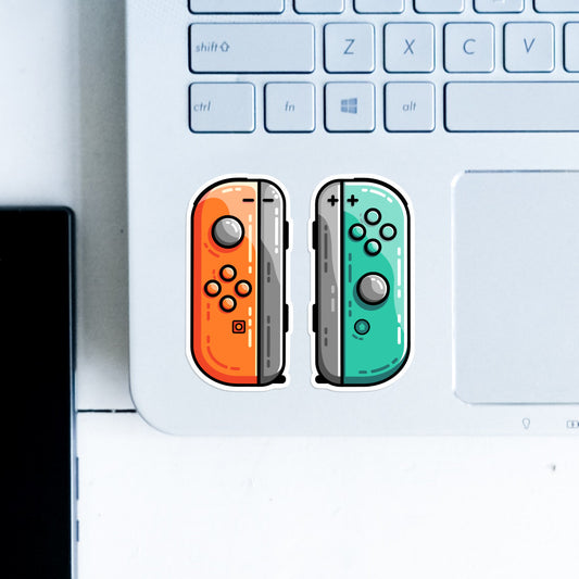 A pair of orange and green gaming controllers stuck side by side on the botto left hand corner of a computer keyboard