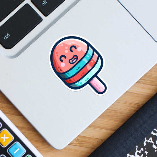 A shaped sticker of a cute red and blue striped ice lolly on a stick with a happy face stuck onto the bottom left hand corner of a laptop computer keyboard