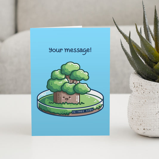 A blue greeting card standing on a white table, with a design of a kawaii cute tree growing in a petri dish and the words above saying 'your message!'
