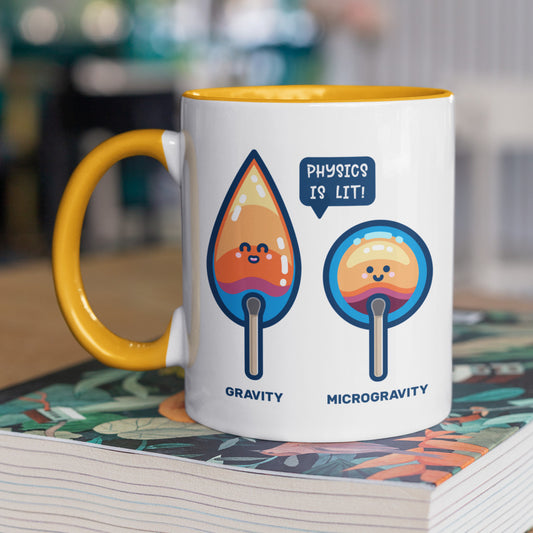 A yellow and white two toned ceramic mug with the handle to the left and a design of two cute flames, one pointed with the word gravity and one circular with the word microgravity and a speech bubble saying physics is lit