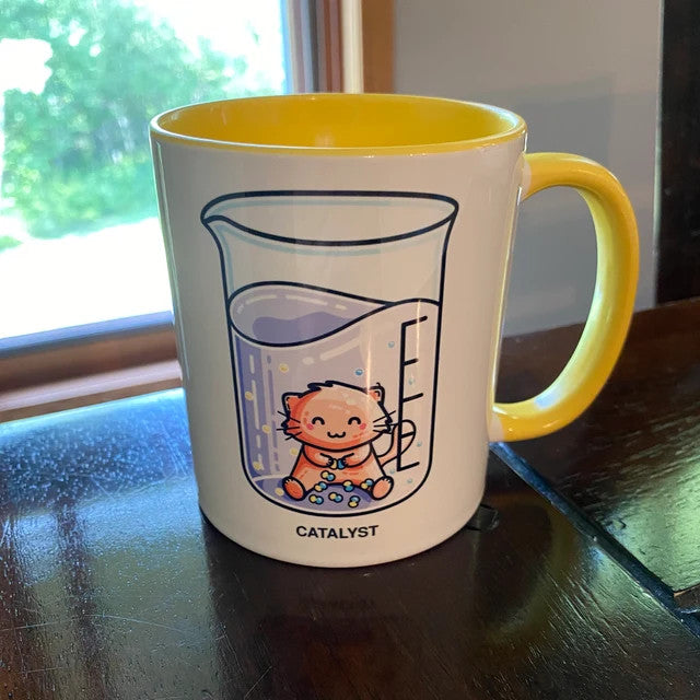 Customer photo of a catalyst pun design printed on a white mug with yellow handle and inside standing on a black surface