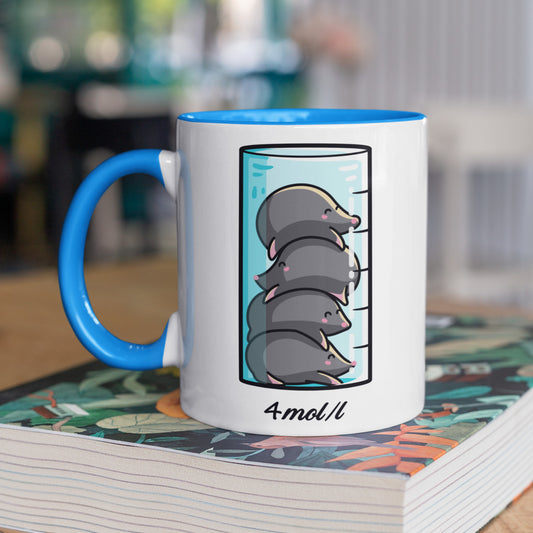 A chemistry beaker filled with 4 cute moles design on a two toned blue and white ceramic mug, shown on top of a magazine