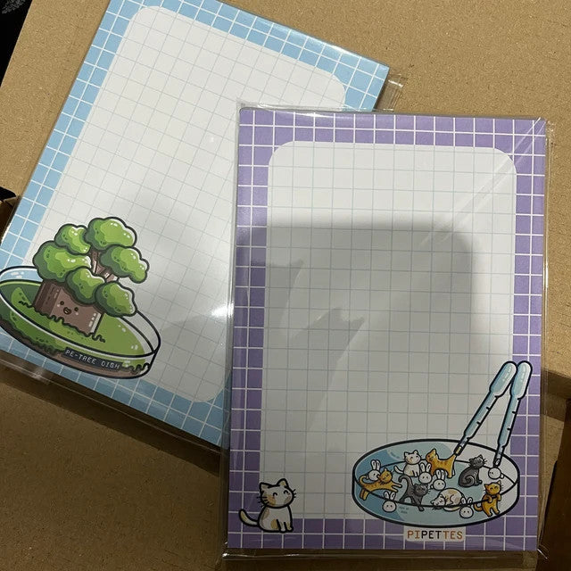 Customer photo of a pipettes pun notepad next to a petri-dish pun notepad lying on top of cardboard packaging