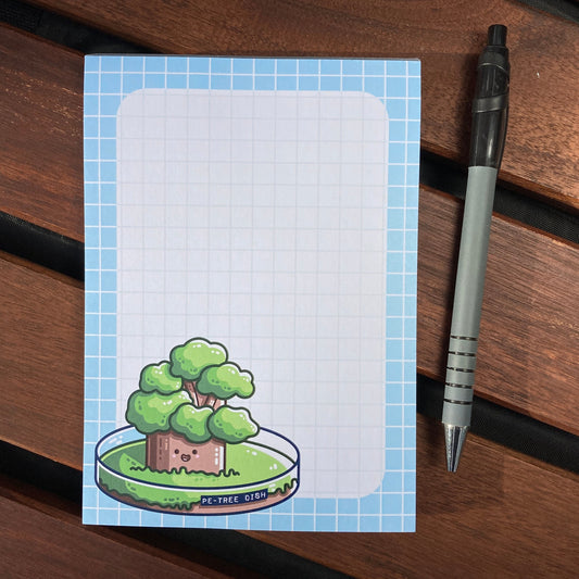 A graph paper notepad with a thick sky blue border and in the bottom left hand corner a design of a kawaii cute tree growing in a petri dish.