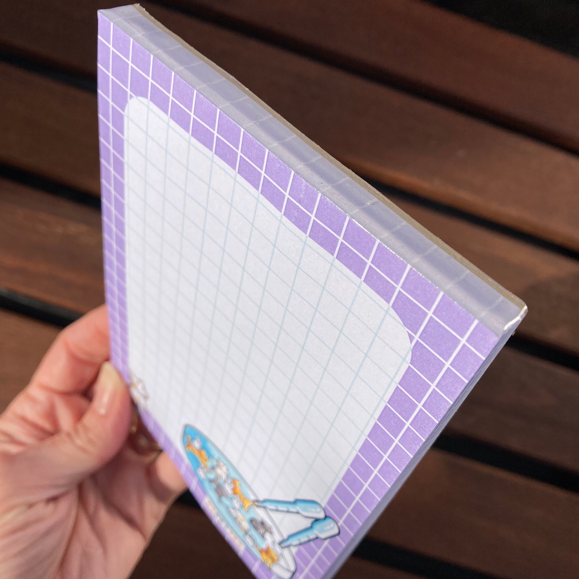 A hand holding the notepad at an angle to show the short top glued edge and a side edge of the notepad.