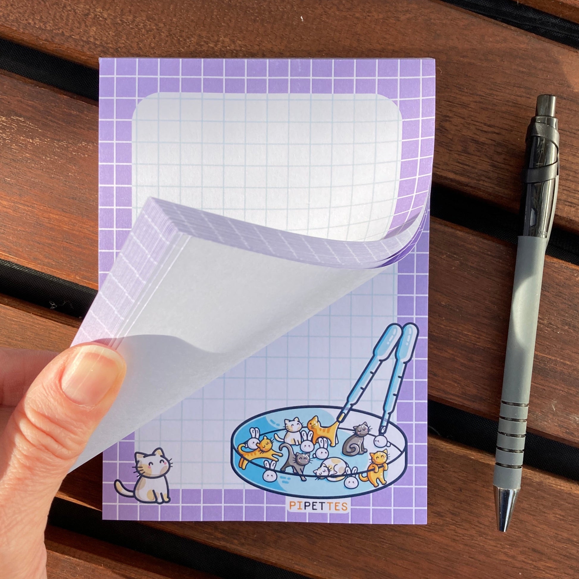 A hand flicking through the pages of the notepad to show that the pipettes design is printed on every tear off sheet.