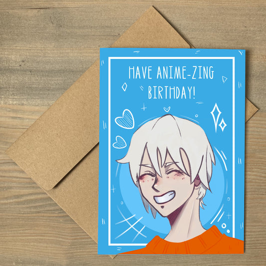 A blue card, flat on a brown envelope, with the head and shoulders of an anime character with a huge smile, blonde hair and an orange jumper. Wording is 'have anime-zing birthday!'