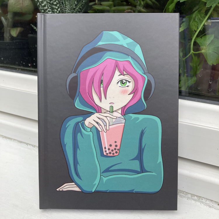 Grey hardback journal standing front facing with a picture of an anime girl with pink hair and green eyes wearing a green hoodie and headphones drinking boba