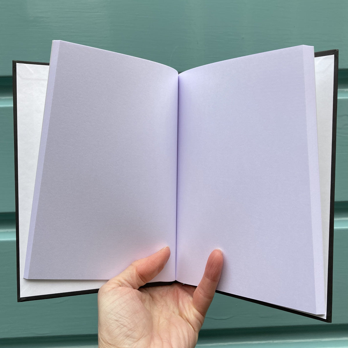 Hardback journal held open in a hand showing plain white pages within