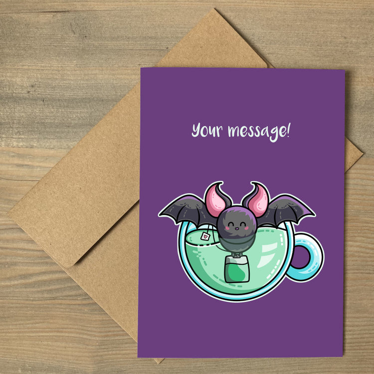 A brown envelope beneath a purple greeting card that features a bat in a cup of green tea with a personalised message above.