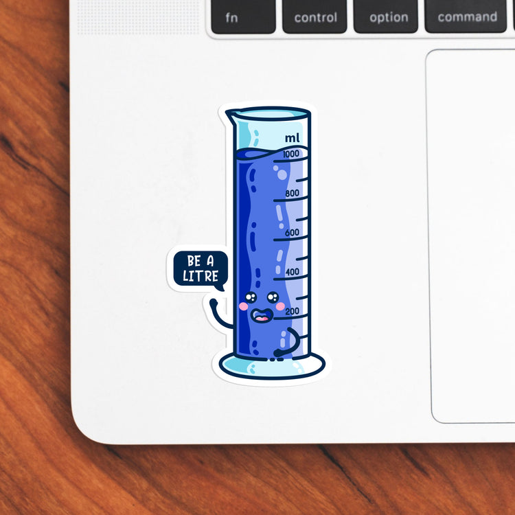 The bottom left hand corner of a laptop computer keyboard with a vinyl sticker stuck to it. The blue sticker is the shape of a graduated cylinder with smily face with a speech bubble saying be a litre.