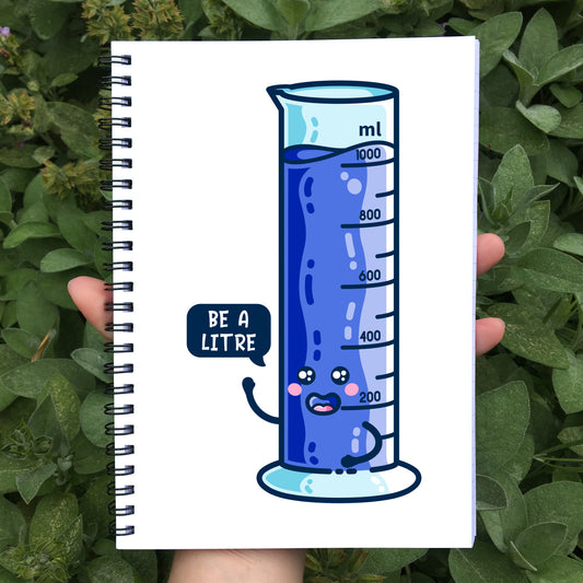 Closed notebook held in a hand with black spiral wire binding, white cover with a blue graduated cylinder saying be a litre in a speech bubble on the front cover