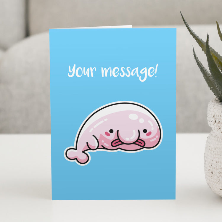 A blue greeting card standing on a white table with a design of a kawaii cute blobfish with a personalised message above.