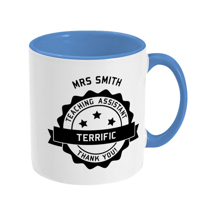 Personalised black circular banner design with the words 'terrific teaching assistant' on a two toned blue and white ceramic mug, showing RHS
