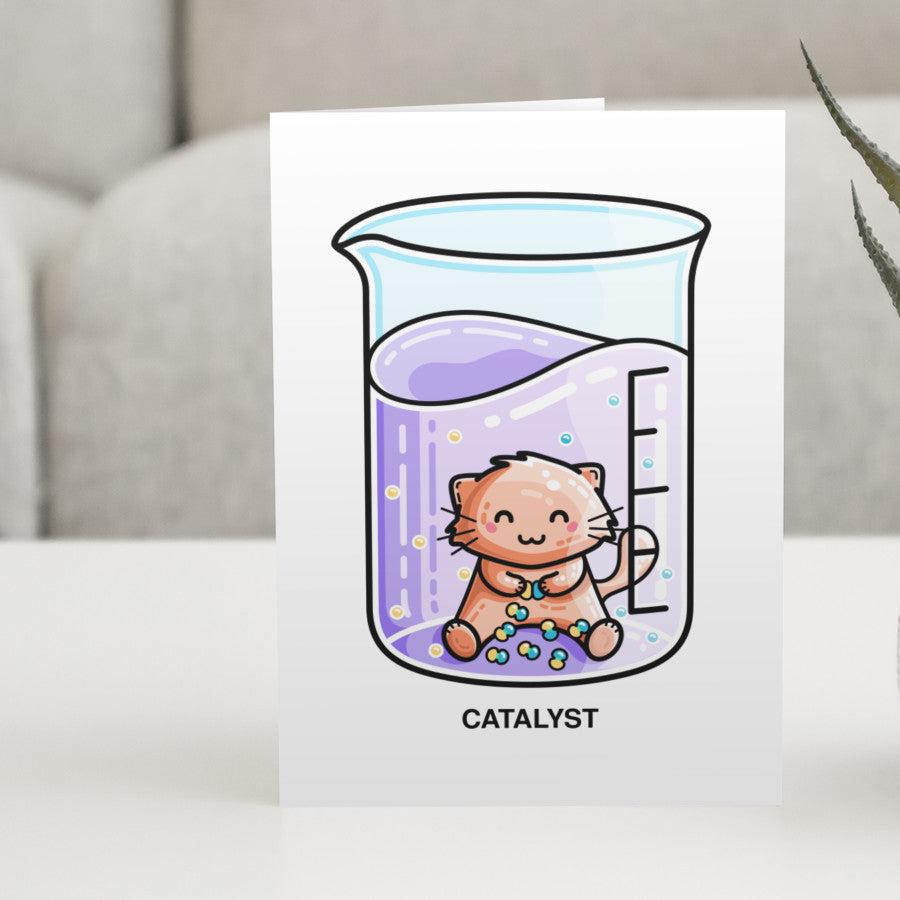 A white greeting card standing on a white table with a design of a cute cat joining atoms in a chemistry beaker of liquid with a personalised message above.
