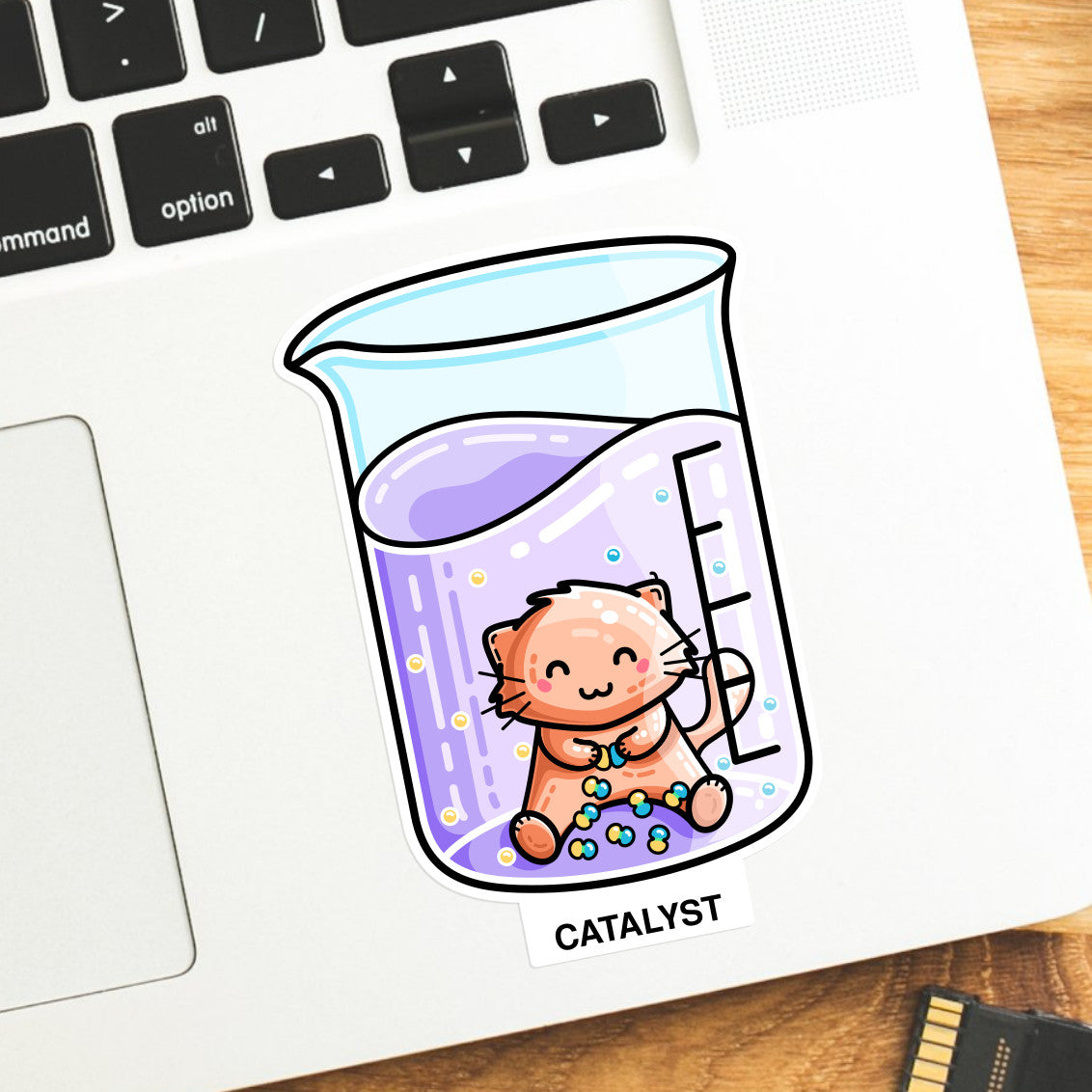 Vinyl sticker of a cute cat in a chemistry beaker joining atoms with the word catalyst, the sticker is on a laptop computer keyboard