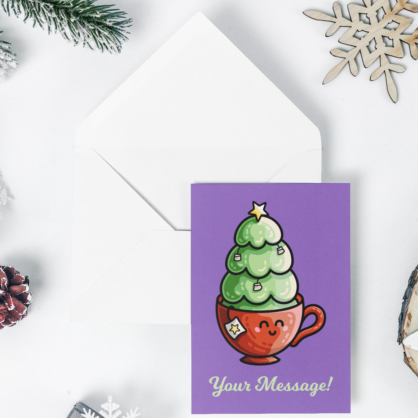 An open white envelope beneath a purple greeting card with a design of a cute red teacup with a Christmas tree planted in it decorated with hanging teabags