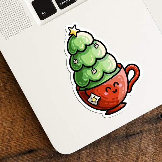 A corner of a laptop keyboard with a die cut vinyl sticker stuck to it featuring a cute red teacup with a Christmas tree planted in it and with teabags and a yellow star decorating the green tree