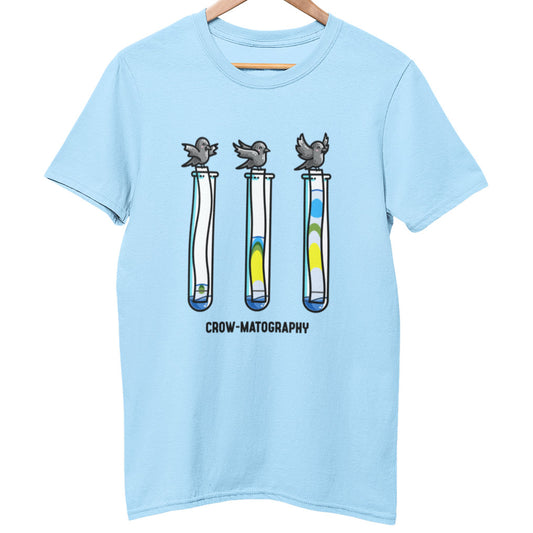 An pale blue unisex crewneck t-shirt on a hanger with a design on its chest of 3 crows holding strips of paper into 3 test tubes showing colour separation.