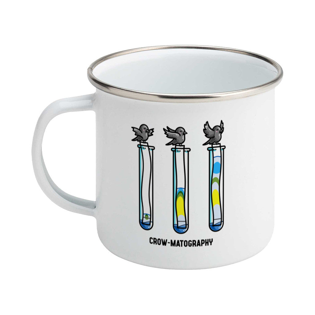 A silver rimmed white enamel mug with the handle to the left showing a design of 3 crows holding strips of paper into 3 test tubes showing colour separation.