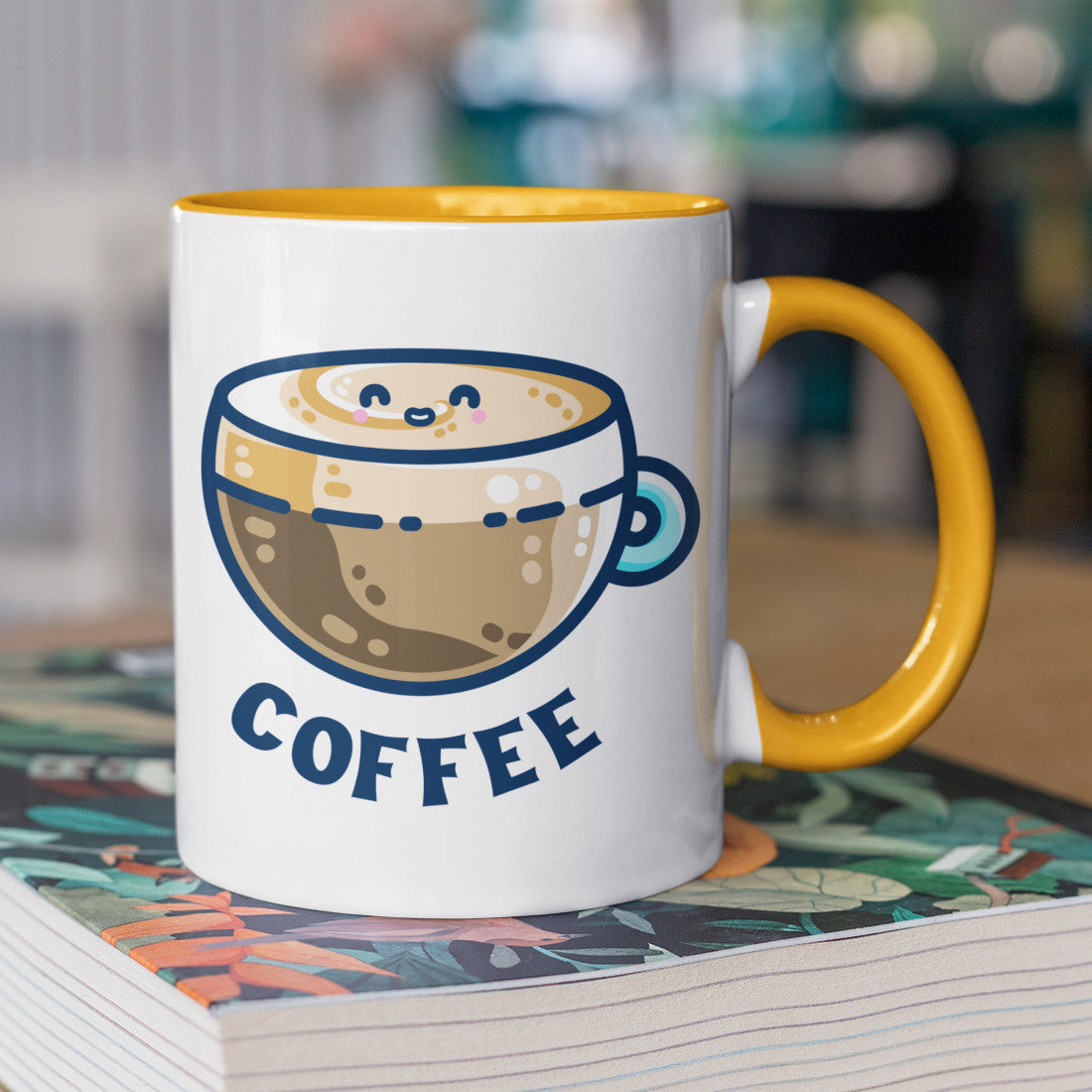 A two toned white and yellow ceramic mug with the handle to the right showing a design of a kawaii cute glass cup of coffee with a thick creamy layer at the top and a smiling face in the cream on the top. The word coffee is in capital letters beneath.