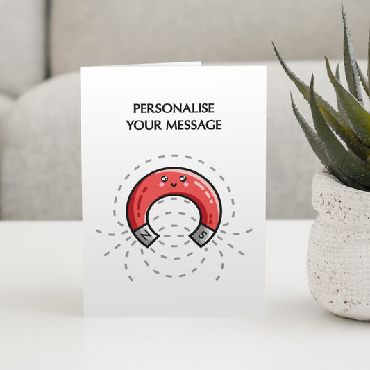 A white greeting card standing on a white table, with the wording 'personalise your message' above a design of a cute red horseshoe shaped magnet and field lines