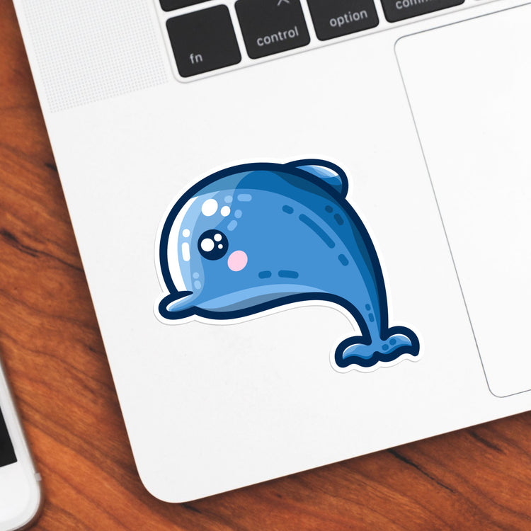 A shaped vinyl sticker of a kawaii cute curvy blue dolphin facing to the left shown stuck onto the bottom left hand corner of a laptop computer keyboard