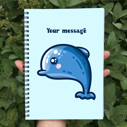 Closed notebook showing the blue front cover with personalised message and cute dolphin design