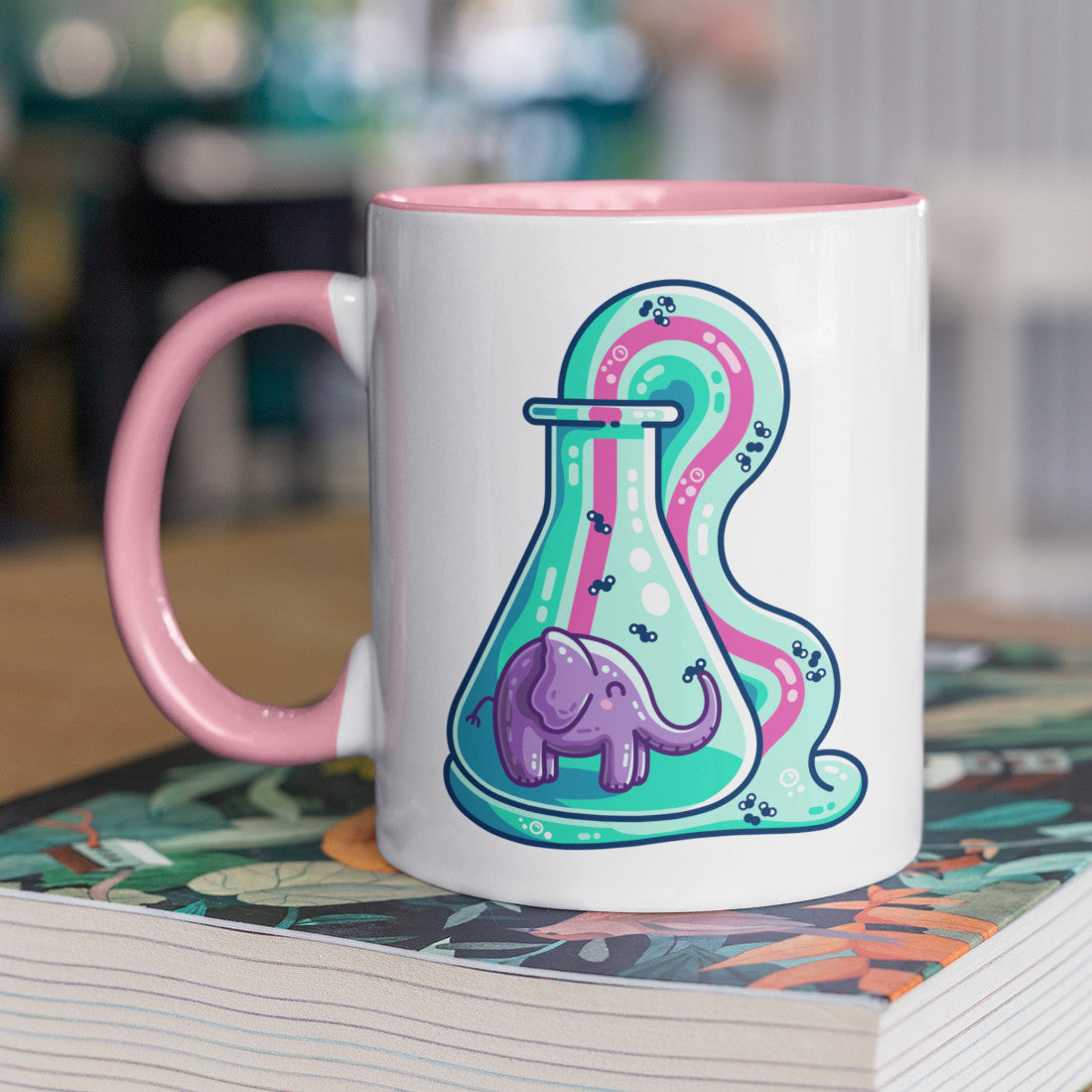 A two toned white and pale pink ceramic mug with the handle to the right showing a design of a conicle flask with a purple elephant inside and green foam coming out and down with a pink stripe along the middle of it with small molecules represented in the foam.