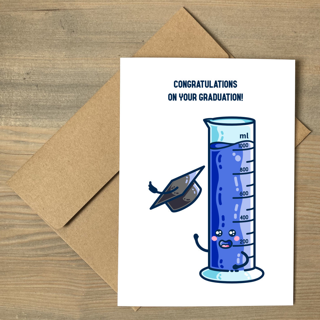 A brown envelope beneath a white greeting card lying flat, featuring a design of a happy one litre graduated cylinder of blue liquid, throwing a graduation cap into the air, with the wording at the top of the card saying "congratulations on your graduation!"