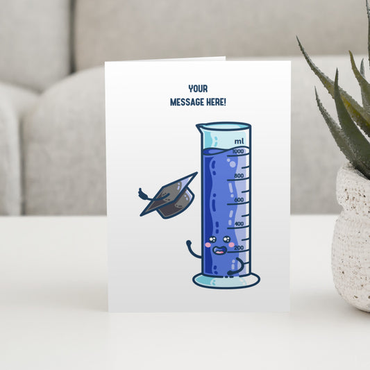 A white greeting card standing on a white table. The card features a design of a happy one litre graduated cylinder of blue liquid, throwing a graduation cap into the air, with the wording at the top of the card saying "your message here!"