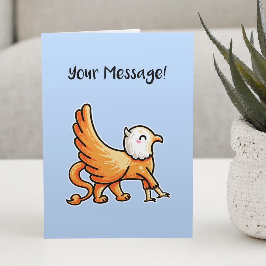 A blue greeting card standing on a white table, with a design of a cute orange griffin walking to the right across the card, with personalised wording above