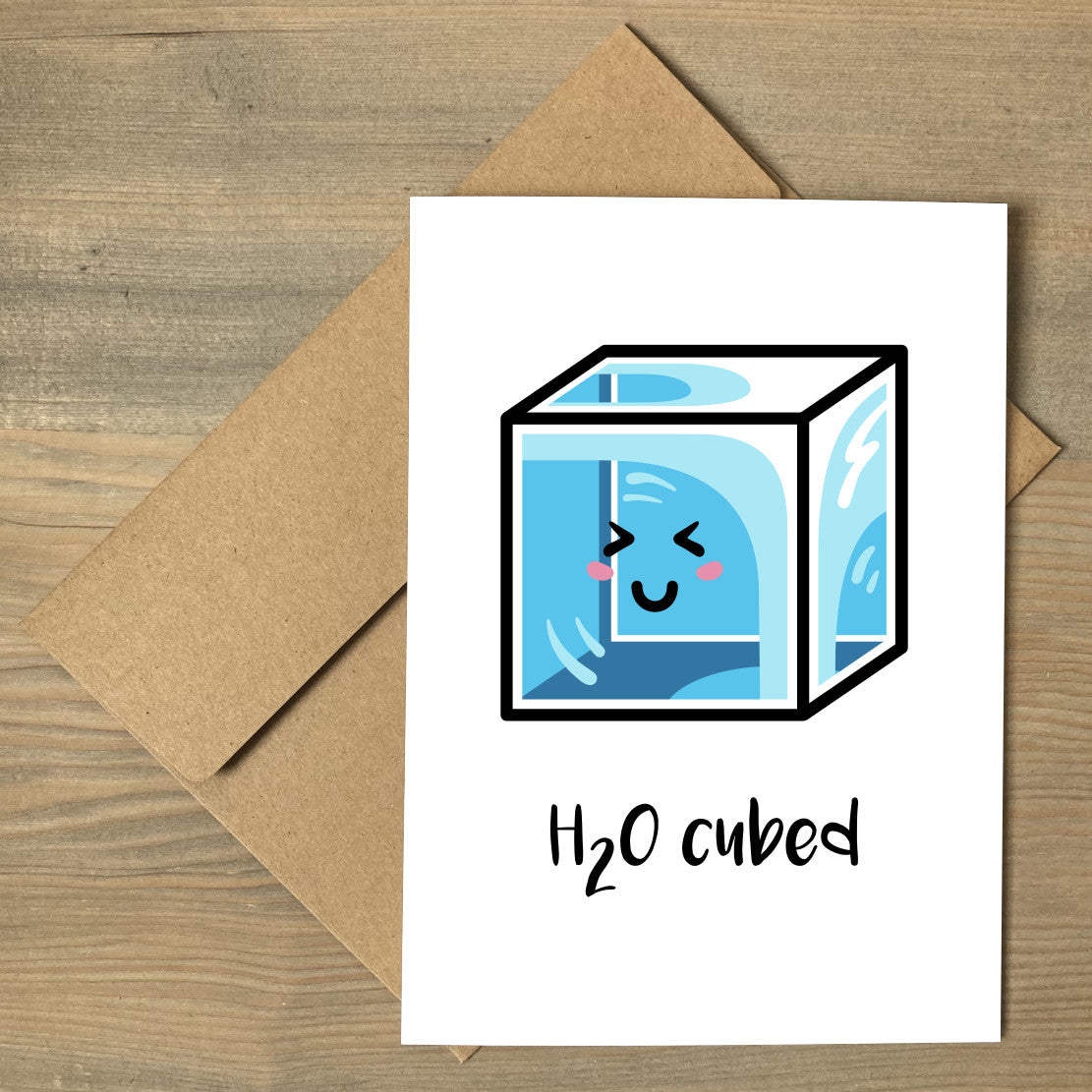 A white greeting card lying flat on a brown envelope, with a design of a kawaii cute blue cube of ice and the words 'H20 cubed'