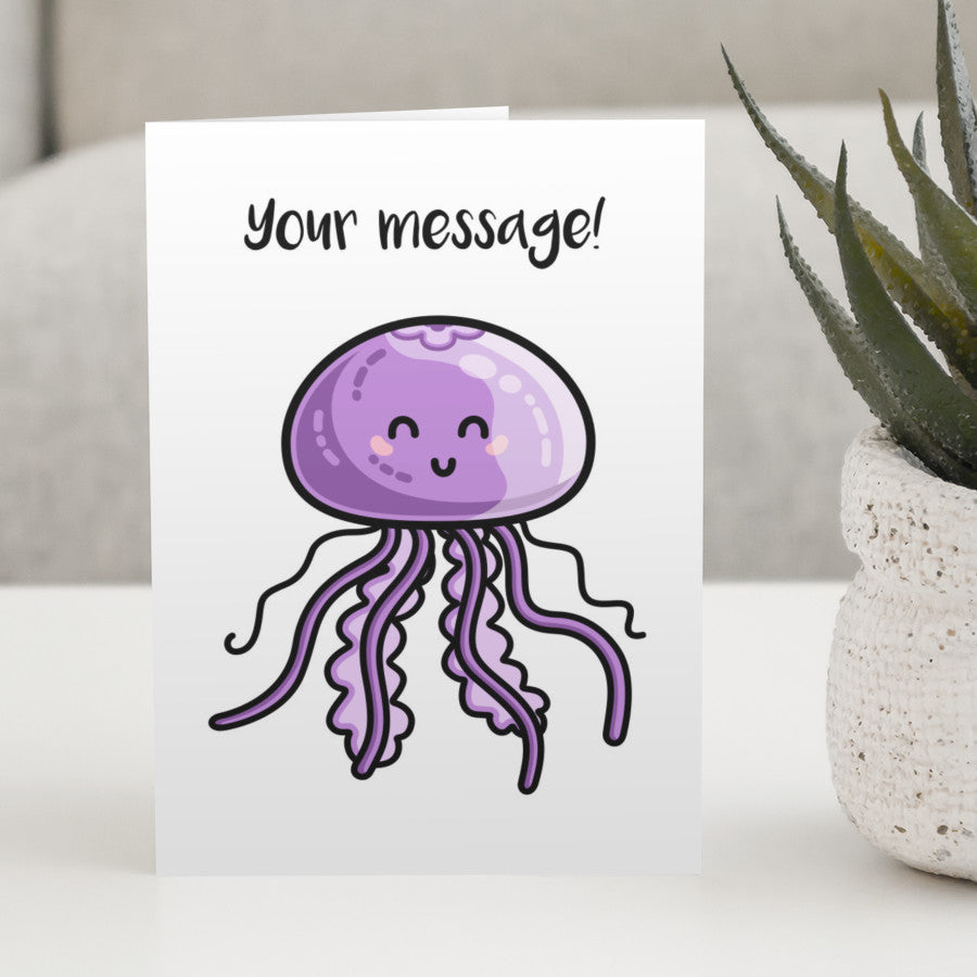 A white greeting card standing on a white table, with a design of a kawaii cute purple jellyfish with a personalised message above