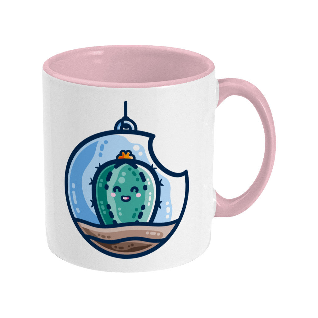 A two toned white and pale pink ceramic mug with the handle to the right showing a design of a kawaii cute happy green cactus succulent planted in a transparent hanging bauble terrarium.