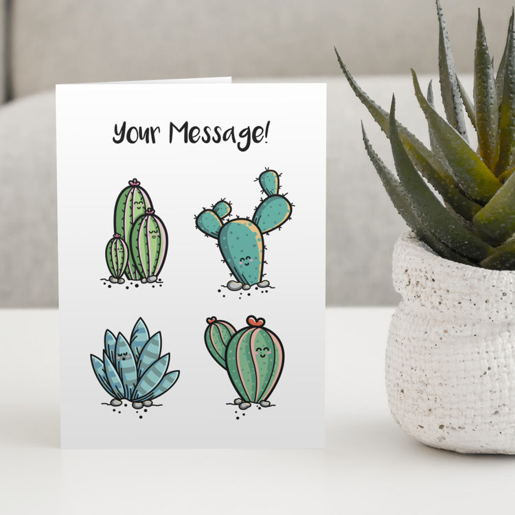 A white greeting card standing on a white table with a design of four kawaii cute cactus plants with the words your message written above