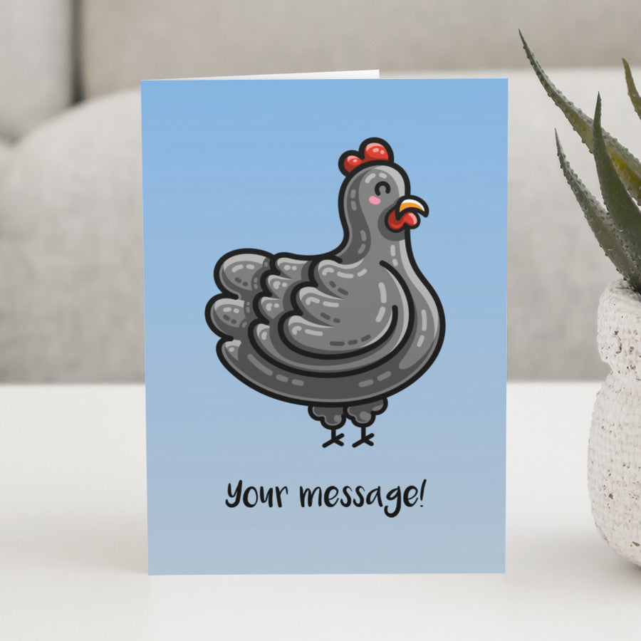 A blue gradient greeting card standing on a white table, with the design of a kawaii cute black chicken and the personalised text 'your message!' beneath