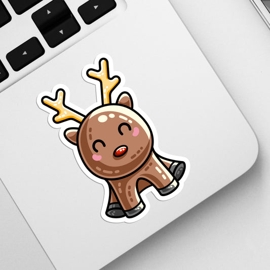 A corner of a laptop keyboard with a die cut vinyl sticker of a kawaii cute red nosed reindeer with yellow antlers in a sitting position stuck on it