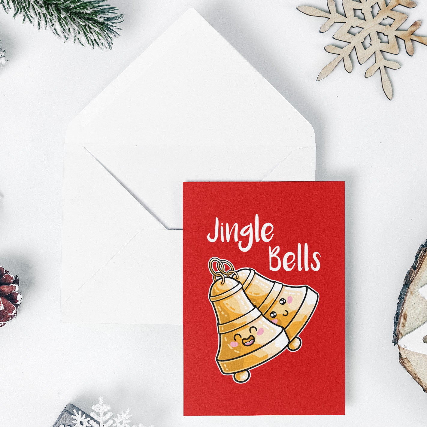 An open white envelope beneath a red greeting card with a design of two kawaii cute bells at an angle and the words 'Jingle Bells' written above