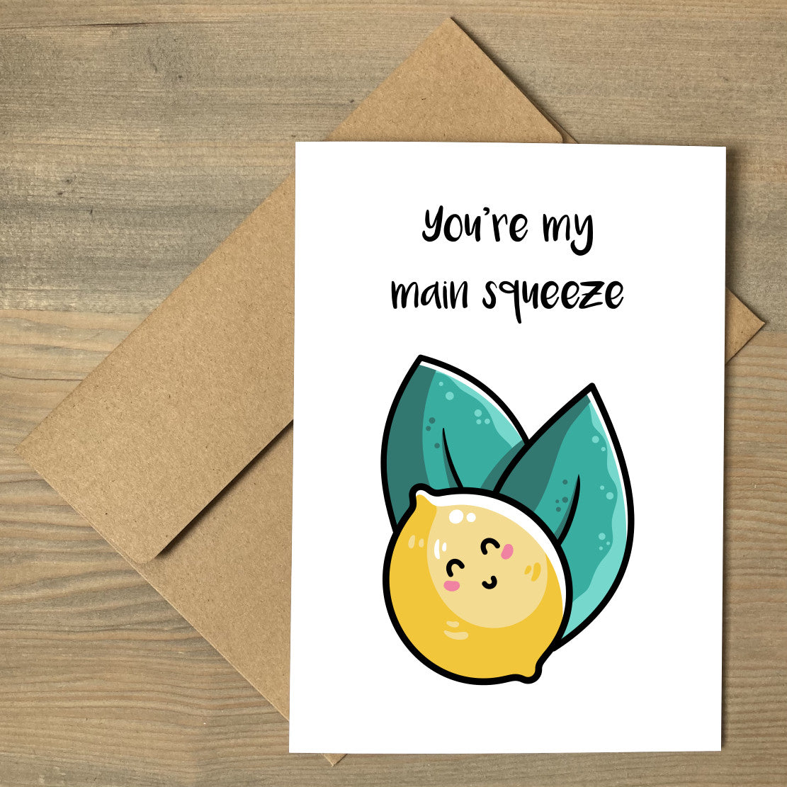 A white greeting card lying flat on a brown envelope, with a design of a kawaii cute lemon and two leaves with the wording above saying you're my main squeeze