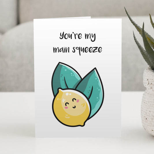 A white greeting card standing on a white table, with a design of a kawaii cute lemon and two leaves with the wording above saying you're my main squeeze