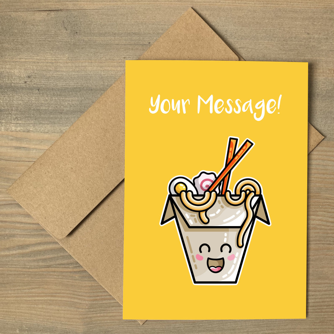 A yellow greeting card lying flat on a brown envelope, with a design of a kawaii cute takeaway box of ramen noodles and chopsticks with a personalised message above