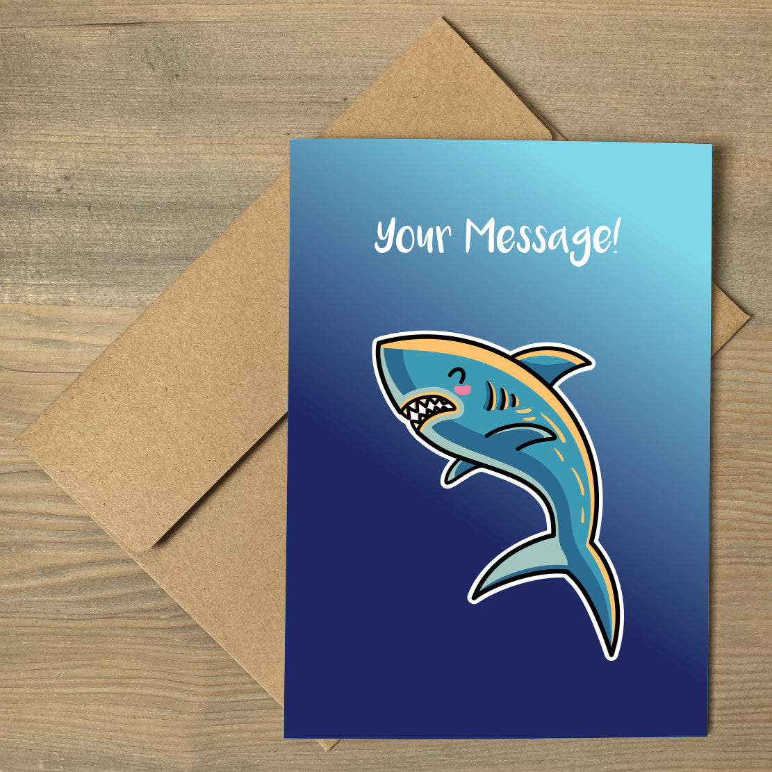 A blue greeting card lying flat on a brown envelope, with a design of a kawaii cute shark with personalised wording above