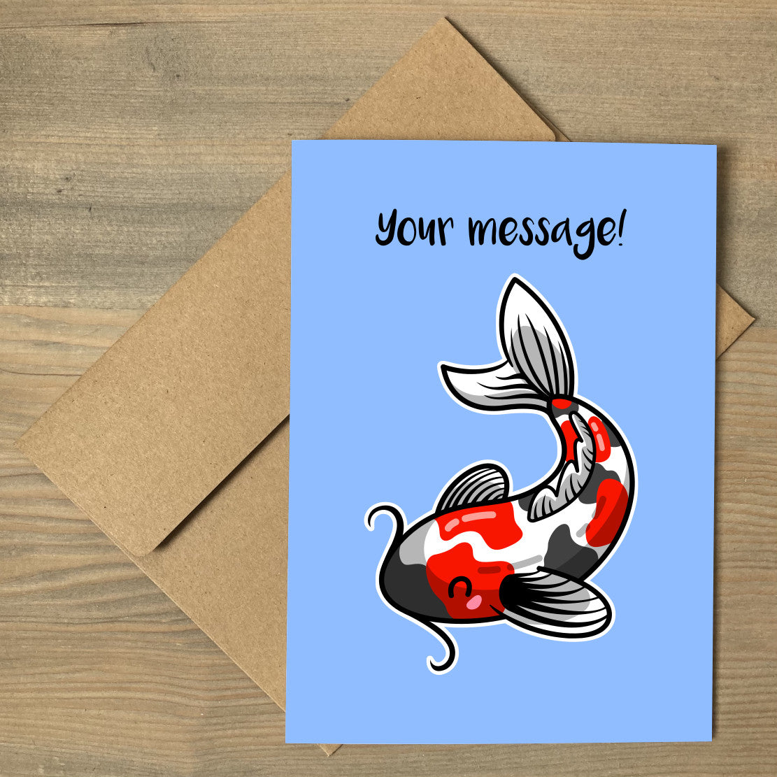 A blue greeting card lying flat on a brown envelope with a design of a red white and grey koi carp fish facing to the left and the words your message written above